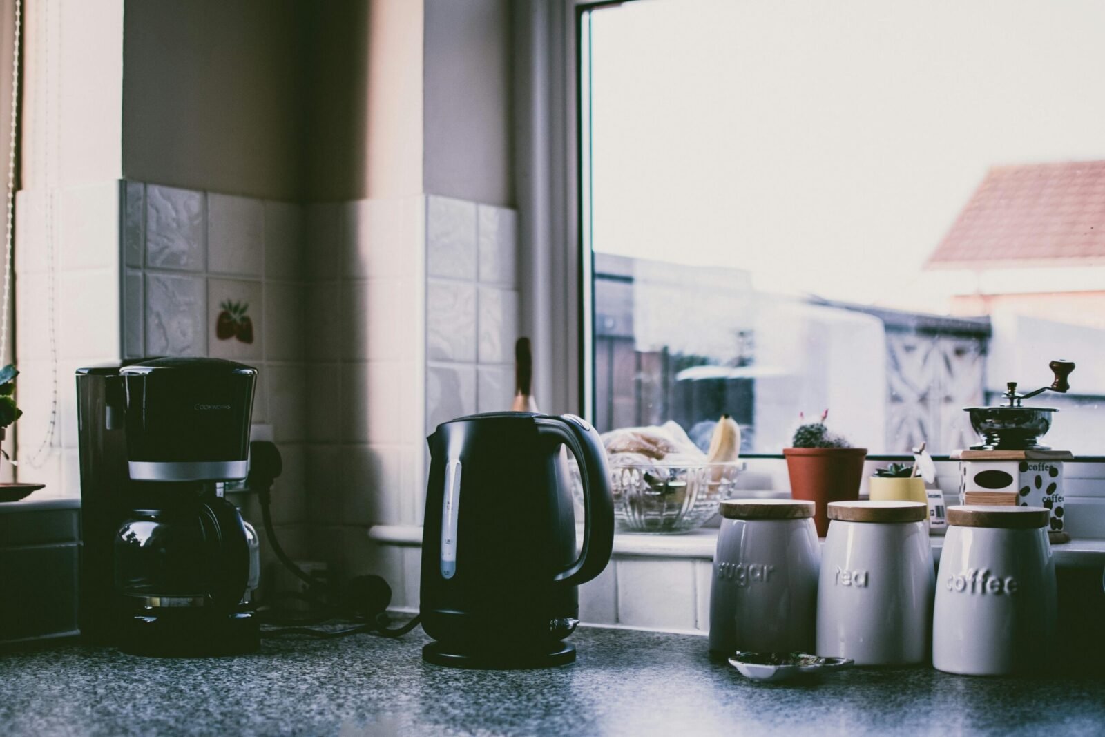 Cozy kitchen scene with coffee maker, kettle, and jars on a sunny counter.